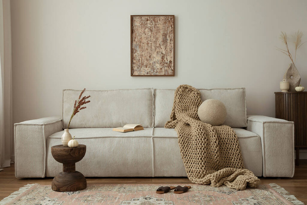 Interior design of living room with mock up poster frame, modern beige sofa, brown braided blanket, wooden coffee table, vase with dried flowers, round pillow, commode, vintage carpet and personal accessories. Home decor. Template. - Photo, image