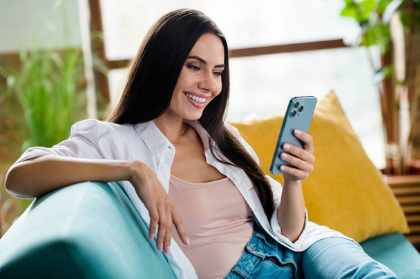 Photo of peaceful lovely cheerful lady sitting comfy couch use smart phone have good mood living room flat indoors. - Foto, immagini