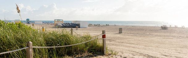 Una playa de arena serena bordeada de una cerca y hierba alta, bajo un cielo brillante, que ofrece una escapada pacífica en la naturaleza. - Foto, imagen