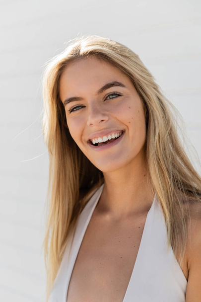 Egy fiatal, gyönyörű szőke nő Miami Beach-en, fehér felsőben, melegen mosolyog a kamerába.. - Fotó, kép