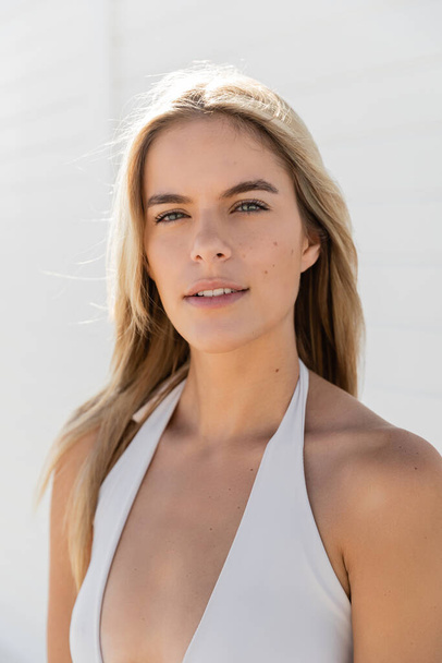 Een mooie jonge vrouw met blond haar poseert vol vertrouwen in een witte top op Miami Beach, uitstralen van gratie en charme. - Foto, afbeelding