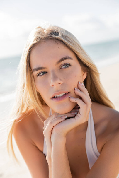 Eine bezaubernde blonde Frau posiert anmutig am sonnenverwöhnten Strand von Miami und strahlt Gelassenheit und Eleganz aus. - Foto, Bild