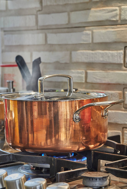 panela de cobre com tampa com prato é cozido sobre o fogo no fogão a gás. O vapor sobe acima do pote. - Foto, Imagem