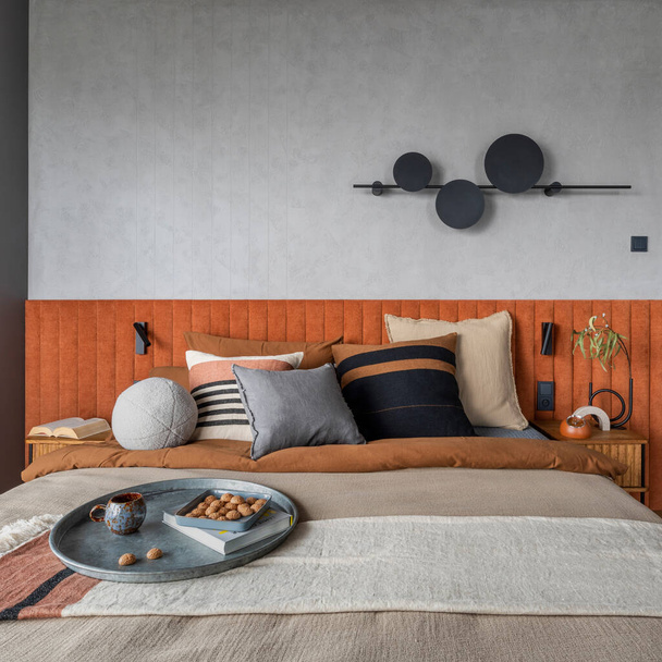 Interior design of elegant bedroom with big orange bed, beige and grey bedclothes, blue curtain, modern lamp, night stand, vase with dried flowers and personal accessories. Home decor. Template. - Foto, immagini