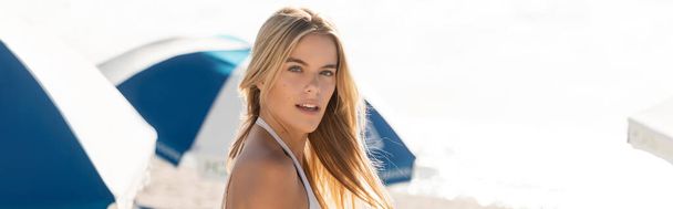 Çekici sarışın bir kadın, Miami sahilinde beyaz bir bikiniyle poz veriyor, zahmetsiz güzellik ve zarafet saçıyor.. - Fotoğraf, Görsel