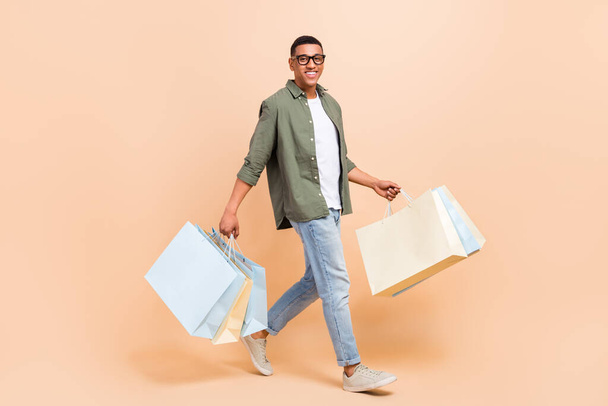 Full length photo of sweet handsome man wear khaki shirt walking holding bargains isolated beige color background. - Zdjęcie, obraz