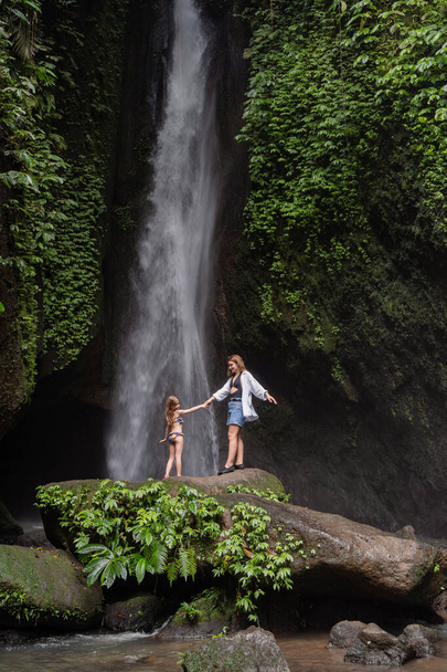 Family at a tropical waterfall. A woman and child at a beautiful waterfall. Vacation on a tropical island. Traveling couple at the waterfall. Family on vacation in Bali - Φωτογραφία, εικόνα