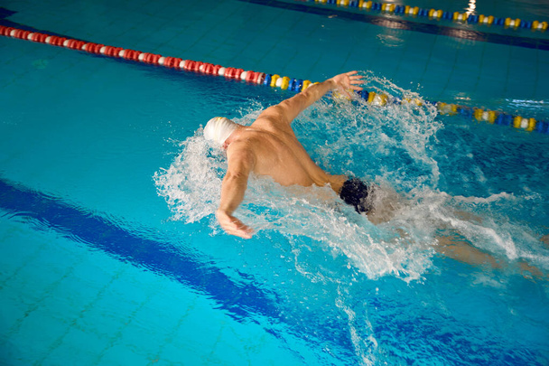 Männchen macht Übungen auf dem Wasser im Stil von Schmetterling, Sportler trainiert im Pool - Foto, Bild