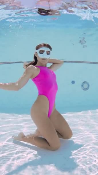 Ελκυστική σέξι γυναίκα με ροζ μπικίνι ποζάρει με μάσκα κατάδυσης κάτω από το νερό στην πισίνα. Πορτραίτο αίγλης - Πλάνα, βίντεο