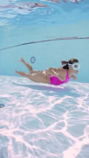 Attraktive junge Frau im rosafarbenen Bikini schwimmt unter Wasser im Pool - Filmmaterial, Video