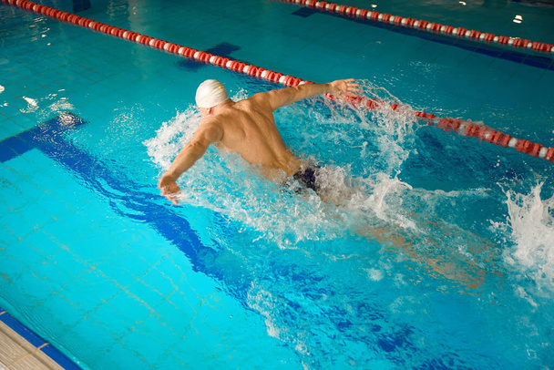 Adult athlete in white cap doing workout for recovery, swimming in butterfly style, resting after work - Foto, Imagem