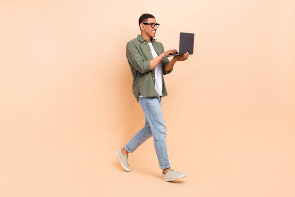 Full size photo of optimistic man wear stylish shirt denim pants look at laptop go to empty space isolated on beige color background. - Φωτογραφία, εικόνα