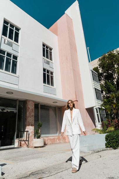 Una giovane, bella donna bionda si trova con fiducia di fronte a un edificio sorprendente a Miami, trasudando raffinatezza e stile.. - Foto, immagini