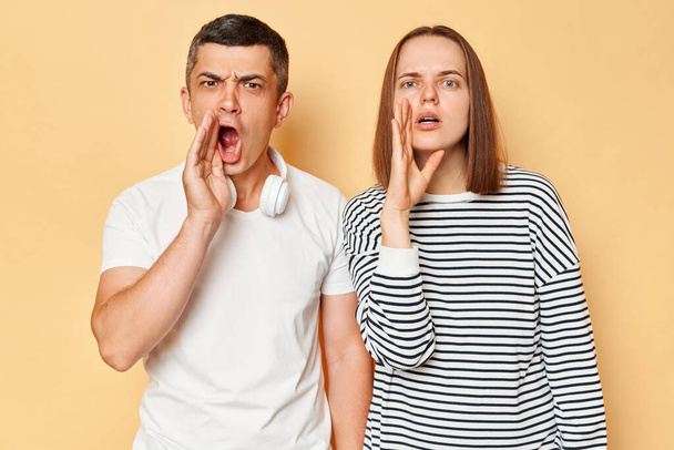 Angry puzzled woman and man wearing casual outfits standing isolated over beige background yelling with hate trying to say important information. - Fotoğraf, Görsel