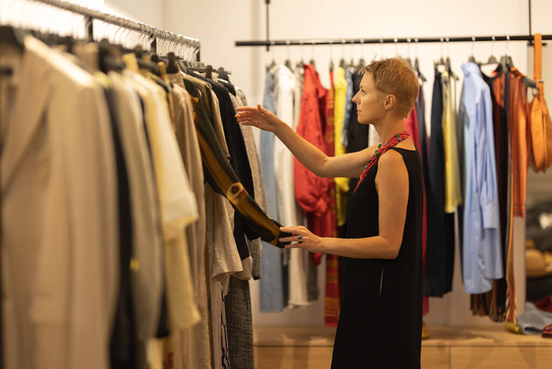 Взрослая стильная женщина смотрит на одежду в бутике. Средний выстрел - Фото, изображение