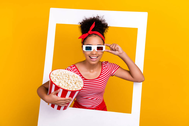 Portrait of excited funky teen girl hand touch 3d glasses hold popcorn box album set card moment isolated on yellow color background. - Фото, зображення