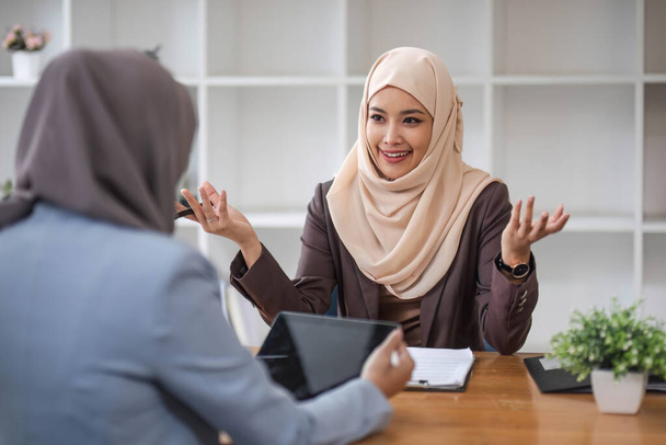 Eine professionelle und selbstbewusste muslimische Geschäftsfrau aus Asien diskutiert mit ihrem Kollegen im Büro über die Arbeit... - Foto, Bild