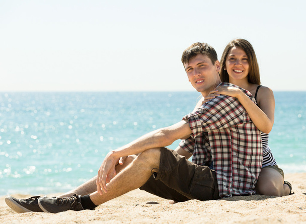 Smiling couple sitting on sand - Фото, изображение