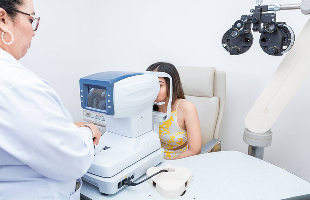 Egy specialista szemvizsgálatot végez egy női betegen. Az autorefraktorral rendelkező beteg látását ellenőrző szemész - Fotó, kép