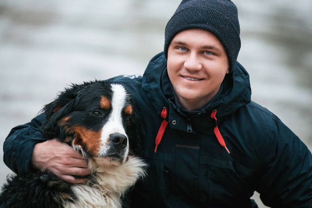 幸せな所有者と若いベルネーゼの子犬。スイス・アルプスにある遊び心のある愛らしい犬と男の肖像画 - 写真・画像