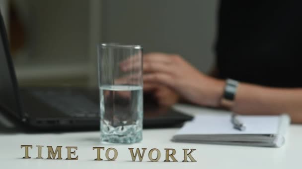 De inscriptie is tijd om te werken, een vrouw werkt op de achtergrond achter een computer, maakt het werk af en vertrekt. - Video