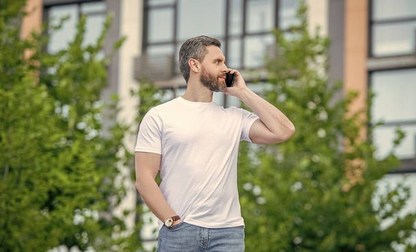 adult man has phone call outdoor. man having phone call in the street. man call on phone outside. photo of man call on phone and talk. - Фото, зображення