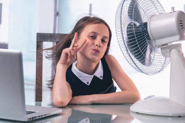 夏の熱波の間、オフィスの机に座って魅力的な若いビジネスの女の子は、彼女は非常に電気ファンで自分自身を冷却するのはうれしいです。水平像. - 写真・画像
