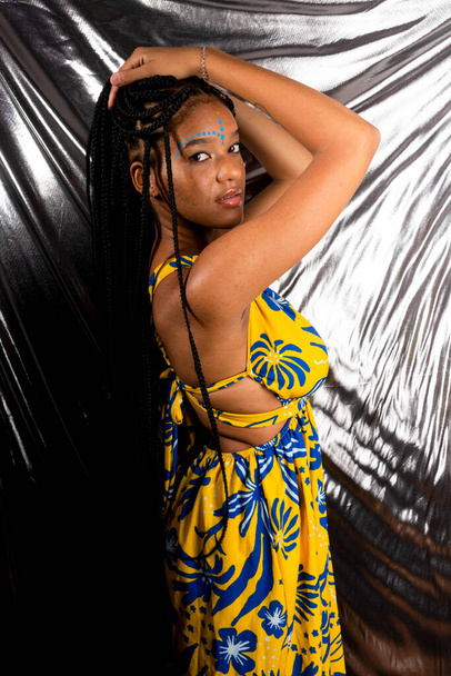 Femme noire, debout, portant des vêtements colorés avec de longues tresses dans les cheveux. Isolé sur fond argenté. - Photo, image