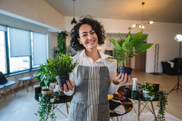 Μία γυναίκα ώριμη καυκάσια γυναίκα σταθεί στο σπίτι με λουλούδια γλάστρα χαρούμενο χαμόγελο μέση μέχρι μπροστά άποψη κηπουρική και βοτανική κηπουρική φροντίδα έννοια αντίγραφο χώρο - Φωτογραφία, εικόνα