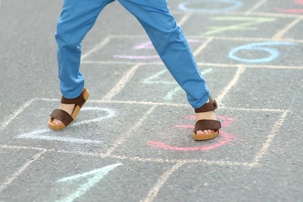 Little boy's legs and hopscotch drawn on asphalt. Child playing hopscotch game on playground on spring day. Outdoors activities for children. - Фото, зображення