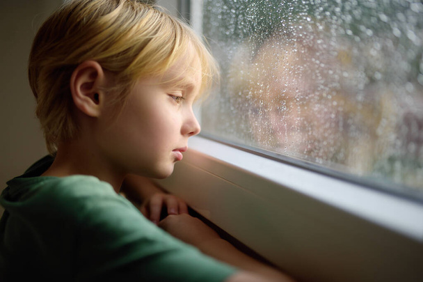Retrato de un triste niño preadolescente de pie junto a la ventana. Niña observando la lluvia afuera. Trastorno postraumático. Alojamiento de duelo. Experimentando pérdida. Miedo. Depresión. Estrés. Muchacho ofendido molesto. - Foto, imagen