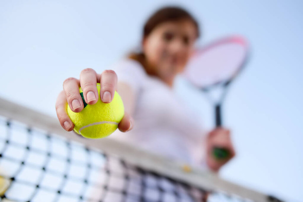 Young female tennis player with tennis ball and racket preparing to serve. Girl on tennis court. Focus on ball. - Photo, image