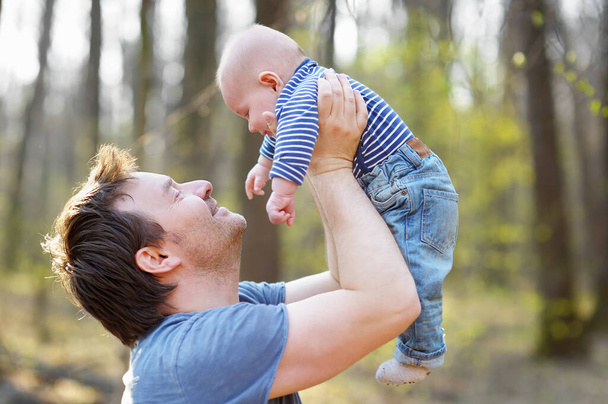 Proud father playing with his newborn son during walking in the park. Happy middle age man tossing his little baby in the air. Parenthood. Involved dad taking care of his infant son - Foto, imagen