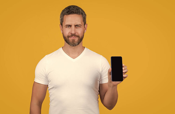 man showing phone screen isolated on yellow background. man showing phone screen in studio. man showing screen of phone. man showing phone screen with copy space. - Photo, Image