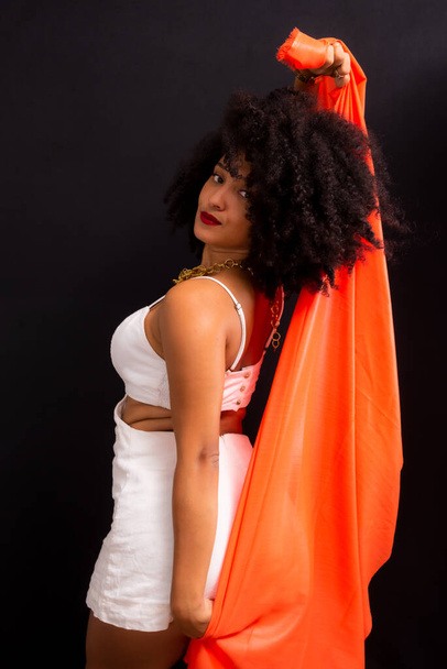 Beautiful young woman with curly hair with an orange cloth over her body. Isolated on light gray background. - 写真・画像
