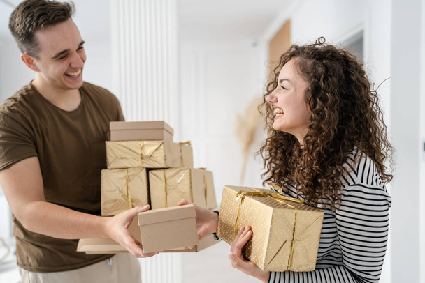 woman young adult caucasian female standing at home with gift box presents holding in hands while her boyfriend or husband man give boxes happy smile real people celebrate surprise concept - Photo, Image