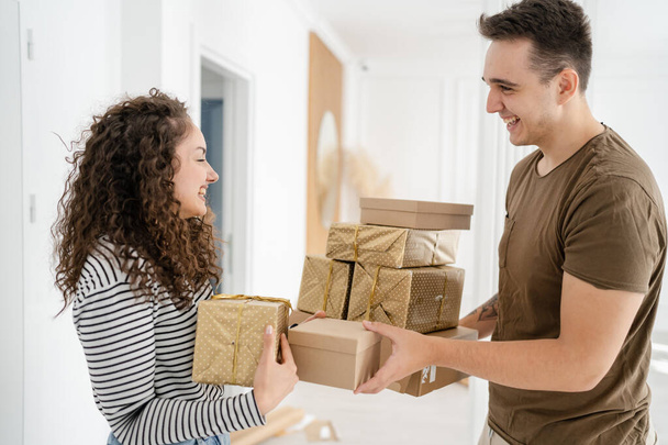 woman young adult caucasian female standing at home with gift box presents holding in hands while her boyfriend or husband man give boxes happy smile real people celebrate surprise concept - Foto, Imagem