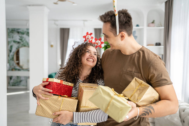 kobieta młody dorosły biały kobieta stojąc w domu z prezent pudełko prezenty trzymając w ręce podczas gdy jej chłopak lub mąż mężczyzna dać pudełka szczęśliwy uśmiech prawdziwe ludzie świętować niespodzianka miłość pojęcie - Zdjęcie, obraz