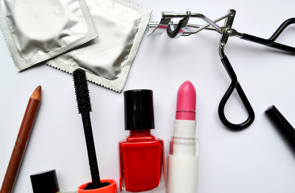 Paar van condooms en een cosmetica bezet met zwarte mascara, roze en rood nagellak en lippenstift en wimper krultang geïsoleerd op wit - Foto, afbeelding