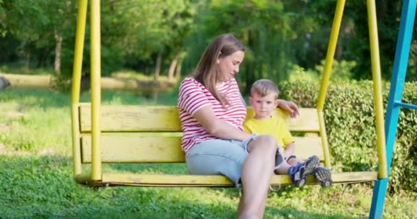Šťastná rodina, matka a dítě houpající se na houpačce v městském parku. Koncept šťastné rodiny, snů, zábavy. Máma a syn spolu. Vysoce kvalitní 4K záběry - Záběry, video