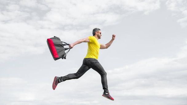 Active man running with sporty bag midair sky background, sport. - Photo, Image