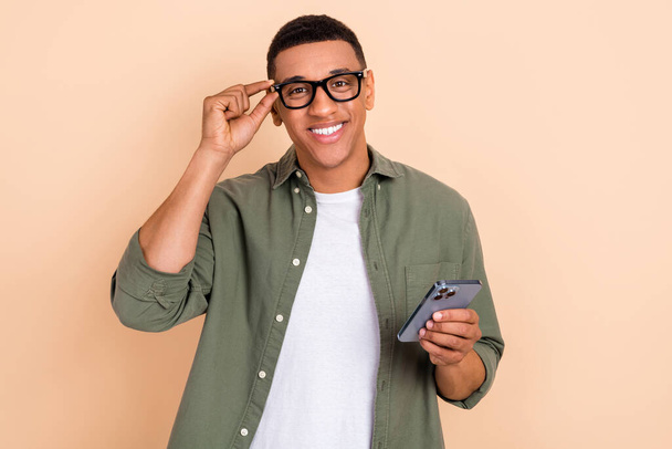Photo of pleasant intelligent smart nice guy dressed khaki shirt touching glasses hold smartphone isolated on pastel color background. - Foto, Imagen