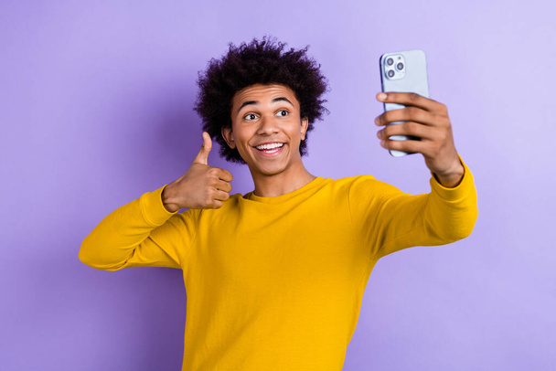 Photo of cheerful handsome guy hold smart phone make selfie demonstrate thumb up isolated on violet color background. - Photo, image