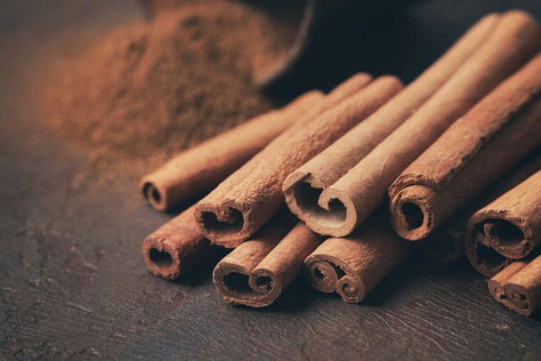 Aromatic cinnamon sticks and pile of sprinkled ground cinnamon on background. Selective focus. - Foto, afbeelding