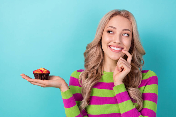 Photo portrait of pretty young girl hold little cupcake bite nail finger wear trendy striped outfit isolated on cyan color background. - Φωτογραφία, εικόνα