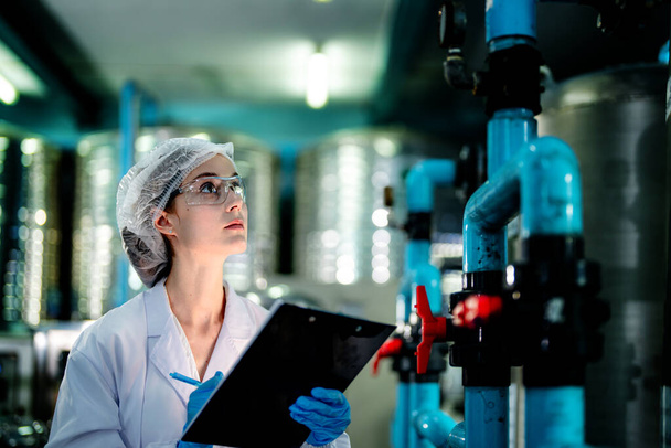 科学者の労働者は、工業工場で逆浸透機械システムの品質をチェックします。制御盤にデータを記録する女性労働者で、可搬型プラントのリサイクル圧力を測定する。. - 写真・画像