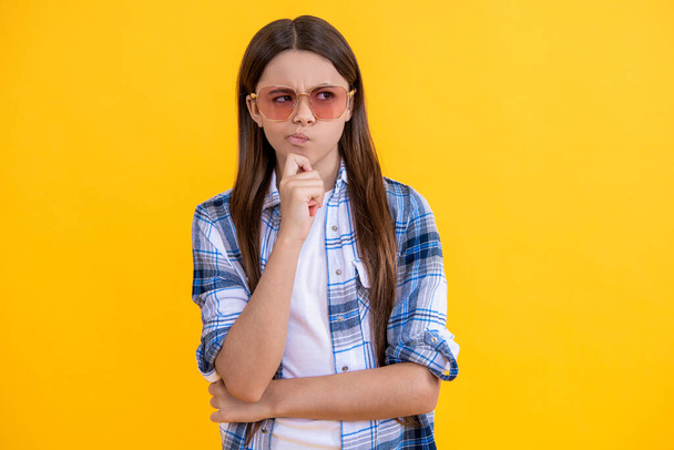Young pondering teen girl standing in sunglasses. Beautiful teen girl wearing checkered shirt. teen girl with long hair. teen girl in casual style. - Фото, изображение