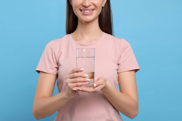 Zdravý zvyk. Happy woman holding glass with fresh water on light blue background, closeup - Fotografie, Obrázek