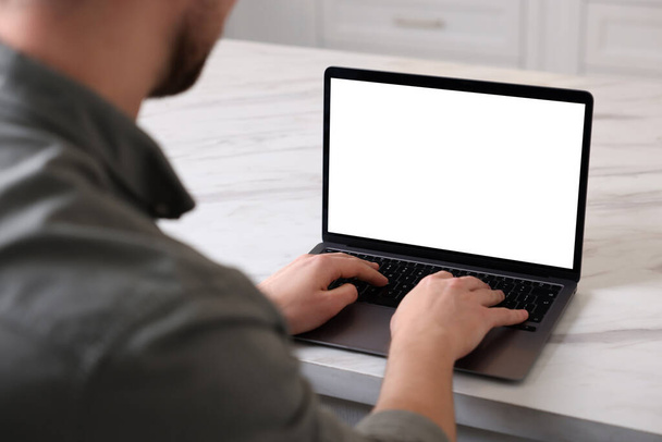 Чоловік працює на ноутбуці на білому мармуровому столі в приміщенні, крупним планом
 - Фото, зображення