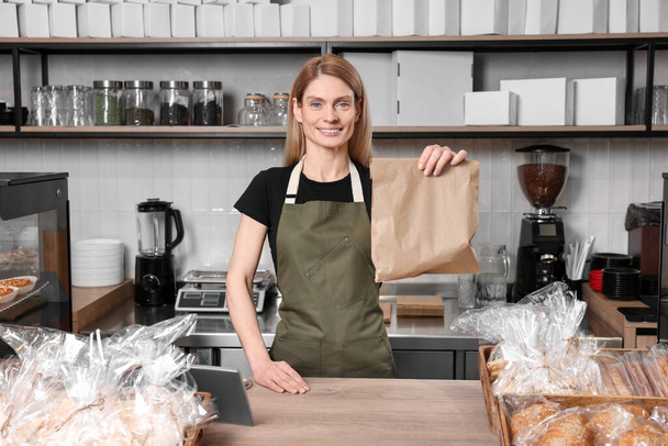 Happy seller with paper bag at cashier desk in bakery shop - Valokuva, kuva